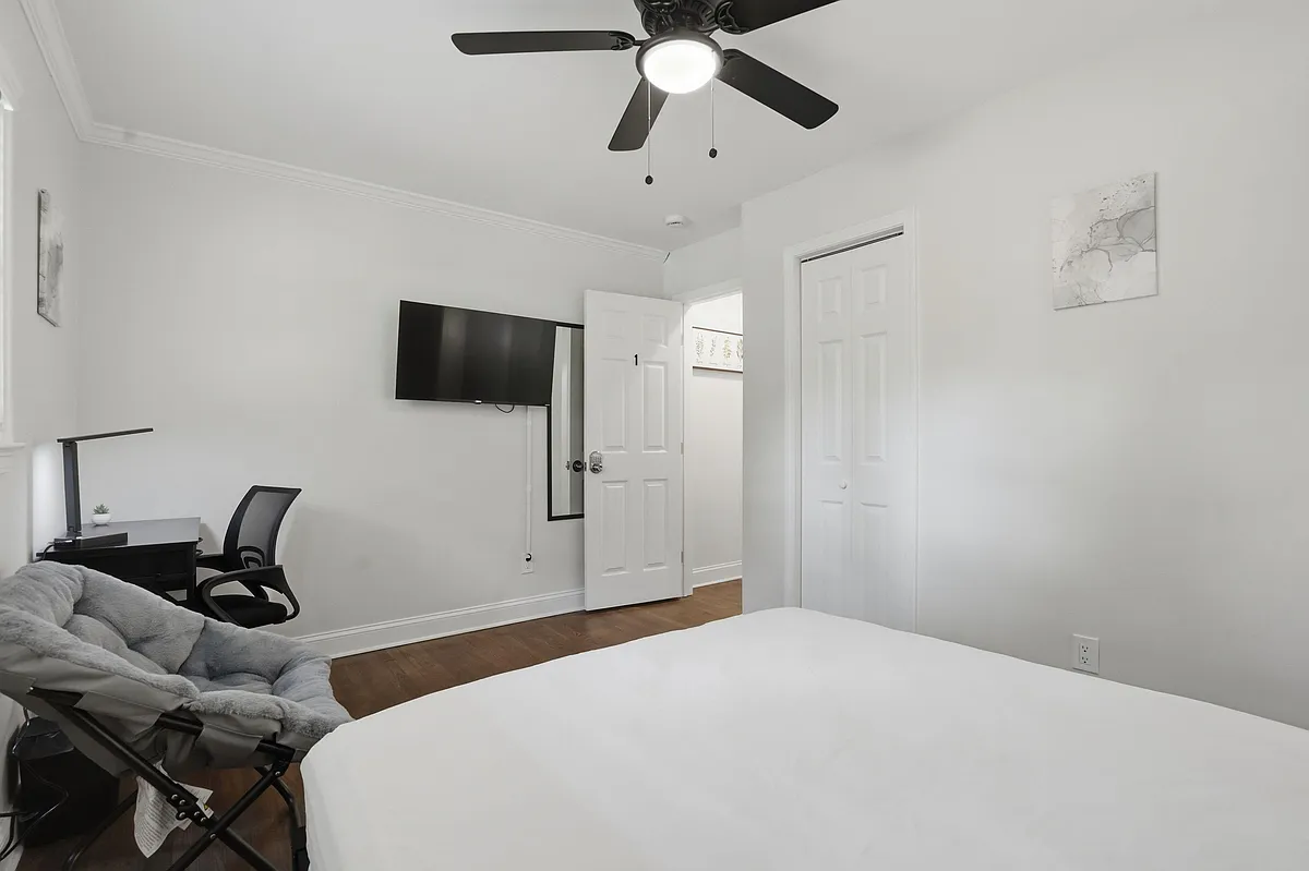 Private bedroom with hardwood floors, ceiling fan, wall-mounted TV, desk workspace, and a closet for convenient storage. - Dodson Dr SW