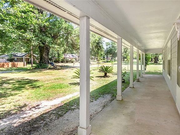Expansive covered porch with multiple support columns, concrete flooring, and a light-toned exterior wall