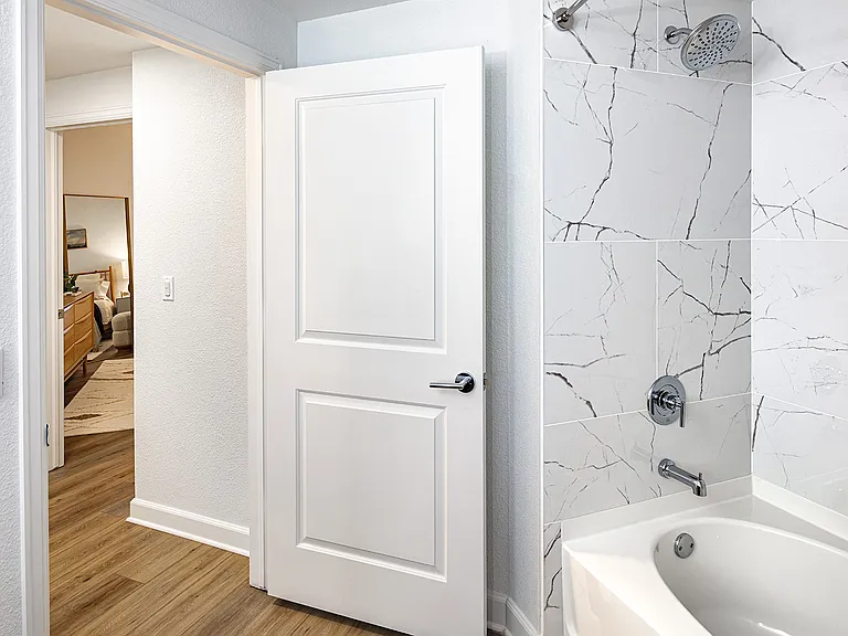 A bathroom with a shower/tub combo featuring a modern white and gray tiled surround.