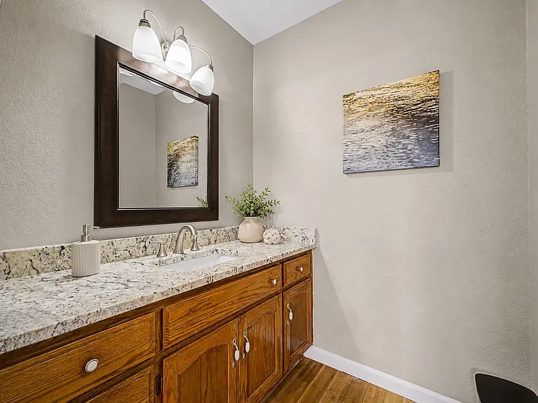 Bathroom vanity with granite-style countertop, undermount sink, ample cabinet storage, and an oversized framed mirror.
