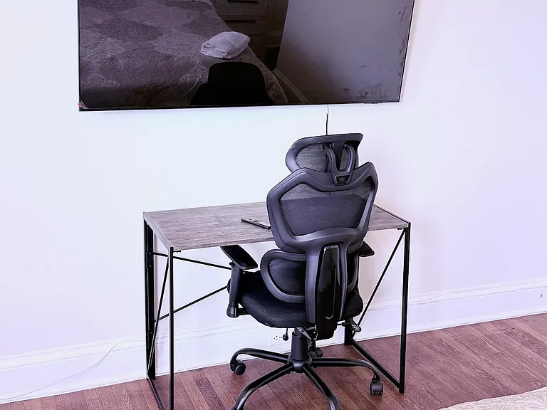 Bedroom workspace area with a desk and ergonomic chair, plus a wall-mounted TV and hardwood flooring for easy upkeep.