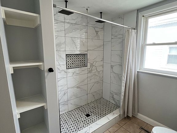 Bathroom. His & Her Shower. Updated full bathroom featuring an oversized tiled shower with multiple shower fixtures, built-in niche, and modern finishes.