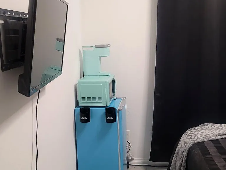 Private bedroom with tile flooring, a wall-mounted TV, and space for a mini fridge and coffee station.
