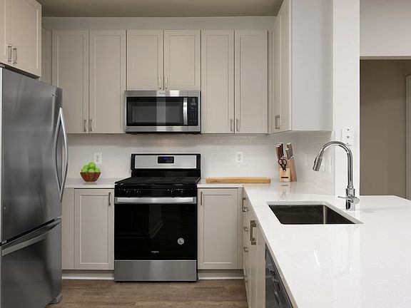 Renovated II kitchen with grey cabinetry, white quartz countertops, stainless steel appliances, white tile backsplash, and hard surface flooring
