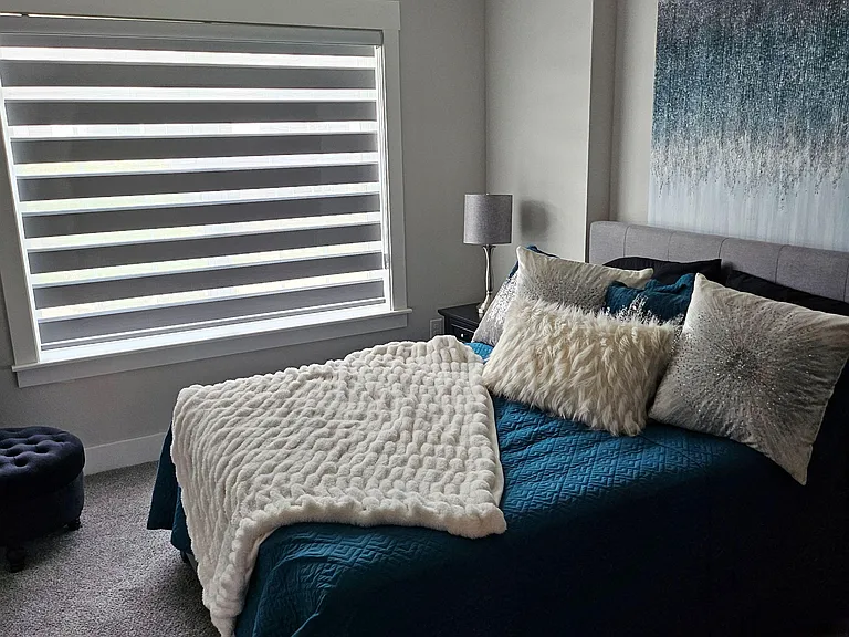 Comfortable bedroom with a large window, ceiling fan, and plush carpeting, offering space with a king size bed.