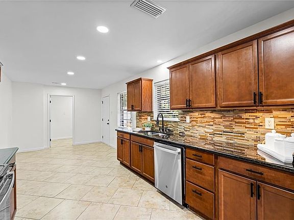Kitchen featuring sink, dishwasher, dark stone counters, and backsplash