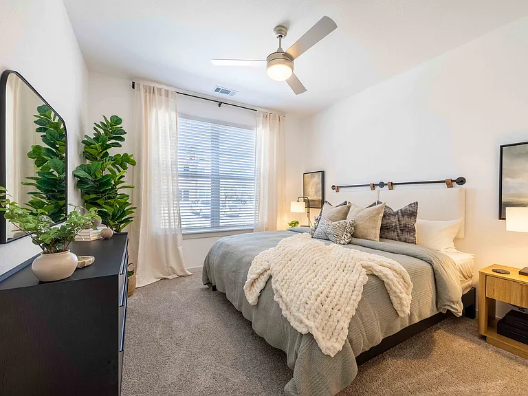 The primary bedroom in this Garrett Parker B1 floor plan includes a queen size bed, wall to wall carpet, and a large window with natural light.