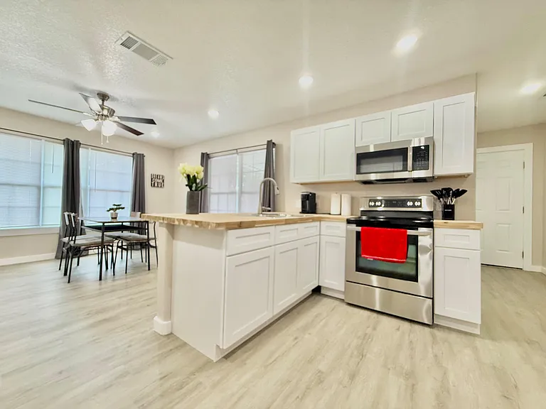 Open-concept kitchen with island seating, ample white cabinetry, and stainless steel range and microwave, plus adjacent dinin