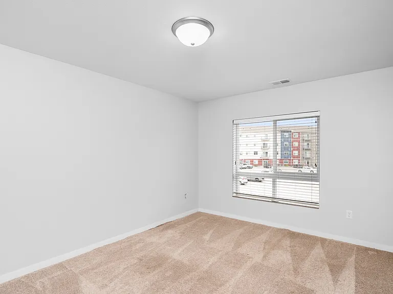Bright and spacious bedroom with plush carpet and a large window offering city views. Bright and spacious bedroom with plush carpet and a large window offering city views.