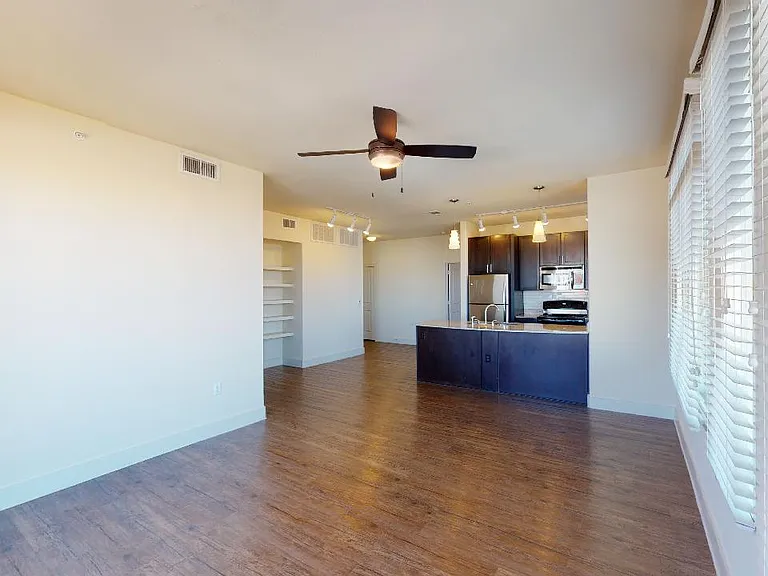 Apartment kitchen with stainless steel appliances, dining and living room with wood-style flooring.