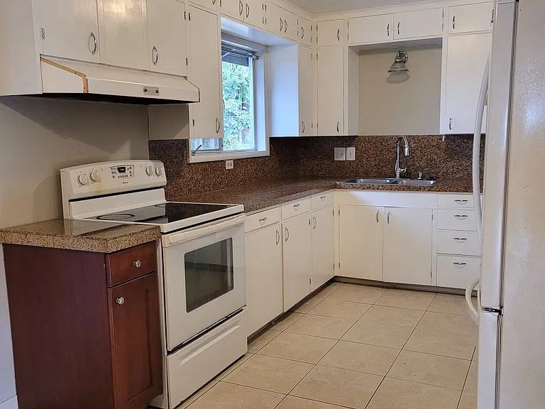 This kitchen has floor to ceiling cabinetry which is newly painted, tile flooring, a high arch faucet, garbage disposal, top french door refrigerator/bottom freezer, a raised dishwasher, and the large window lets in lots of light.