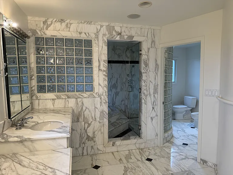 In-suite primary bathroom is tastefully appointed with glass block walls featuring dual sinks, Jacuzzi tub, multi-jet shower stall, a bidet, and a walk-in closet with built-in organized storage.