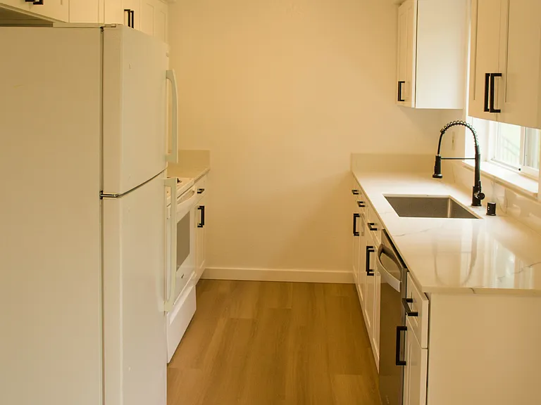 Bright galley-style kitchen with brand-new cabinets, updated flooring, modern finishes, and natural light from the large window.
