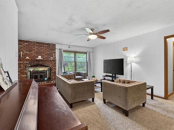 Living room view from entryway featuring a brick fireplace with an insert, white vertical paneling, carpeting, and a ceiling fan with integrated lighting