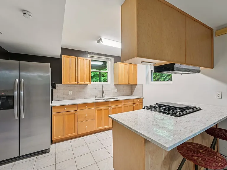 A warm and functional lower level kitchen where honey toned cabinetry, sleek counters, stainless steel appliances, and leafy window views create a charming space for everyday ease.