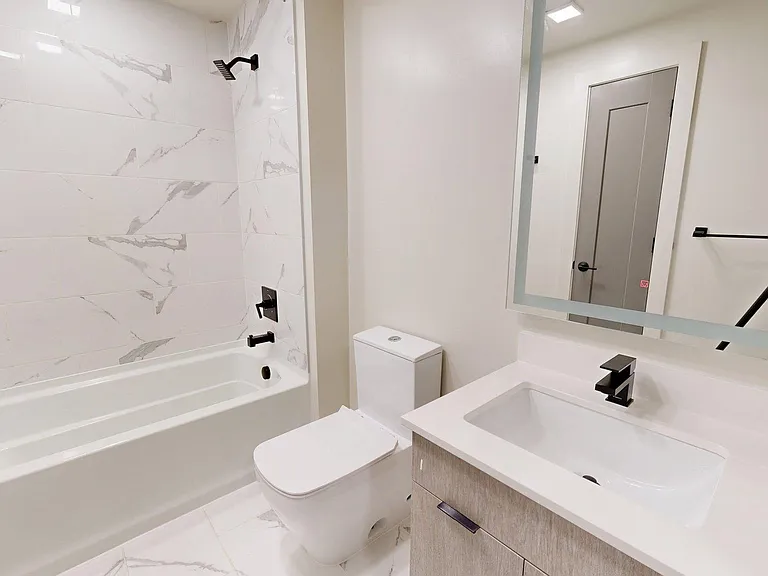 Apartment Bathroom with large soaking tub, LED vanity mirror and tiled flooring.