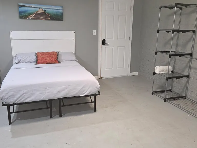 Furnished bedroom with full-size bed, nightstand and lamp, plus open shelving for convenient storage and organization.