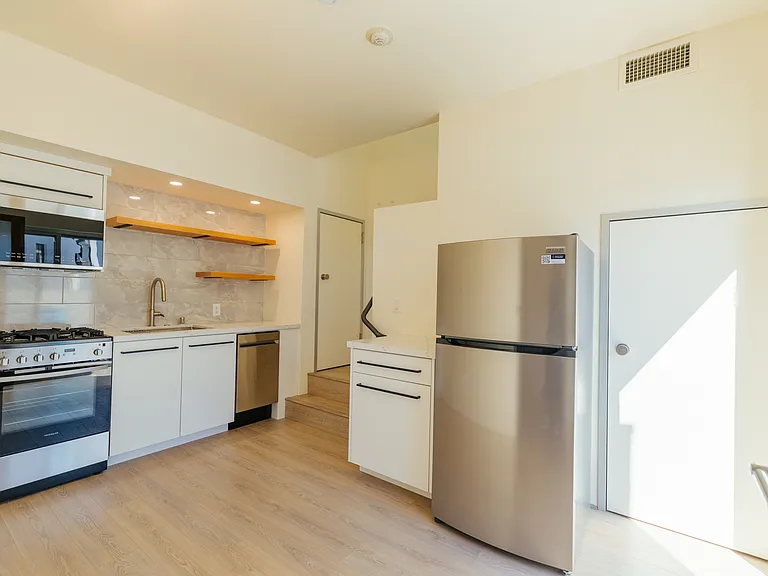 Fully renovated kitchen with view to the staircase to the second floor. Door on the right is to storage. Custom cabinetry, tiled backsplash. Includes stove, oven, microwave and dishwasher.