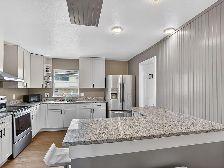Updated kitchen with granite counters, ample cabinetry, and stainless appliances including a side-by-side refrigerator.