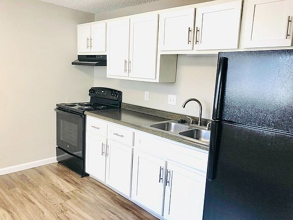 Modern kitchen with sleek black appliances, stylish white cabinetry, and elegant wood flooring.
