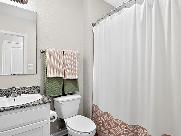 Modern bathroom featuring a sleek granite countertop, elegant sink, and cozy neutral decor with matching plush towels and a clean white shower curtain.