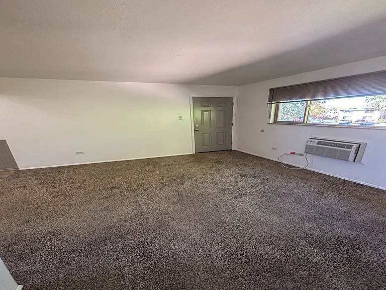 Inviting living room with plush carpet, natural light through a large window, and a modern air conditioning unit for comfort.