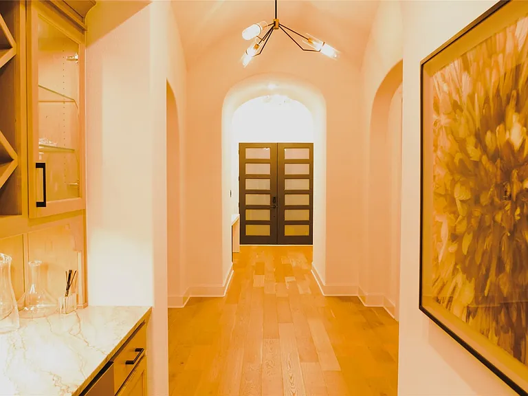 Hallway featuring light wood-finish flooring, arched doorways, a geometric chandelier, and built-in cabinetry with a wine rack and stone countertop