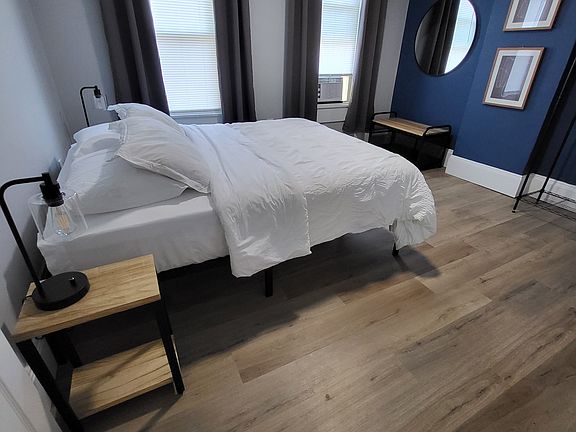 Main bedroom has a queen size hybrid mattress, blackout shades, bedside lighting, and modern open storage.
