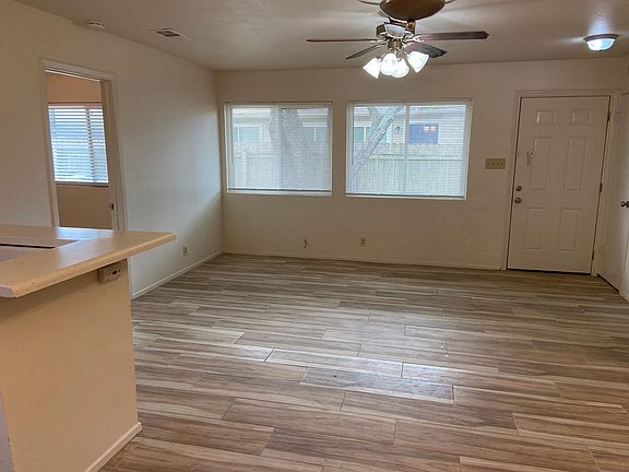 Open living area with ceiling fan and large windows. Tile floor not as pictured.