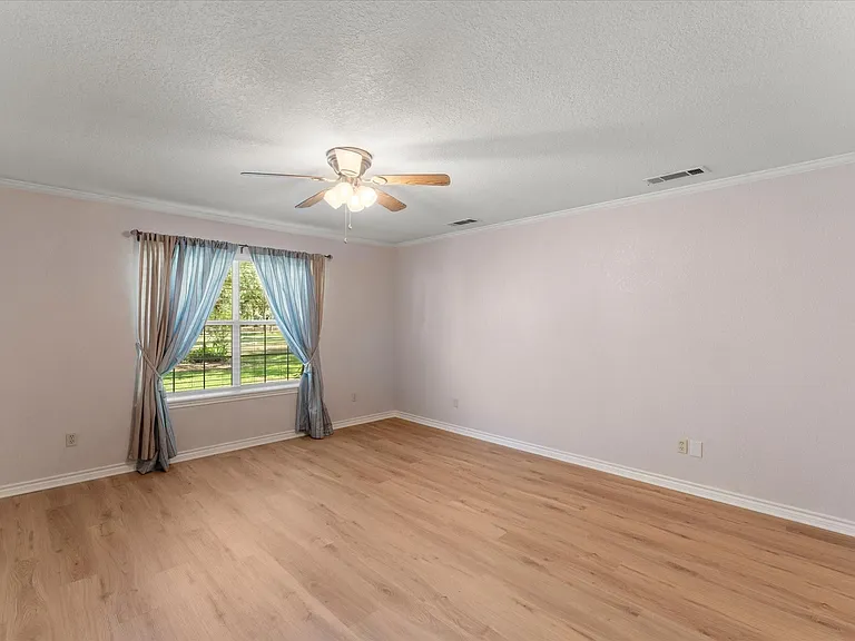 Spacious room featuring wood-finish flooring, a ceiling fan with integrated lighting, and a window providing natural light