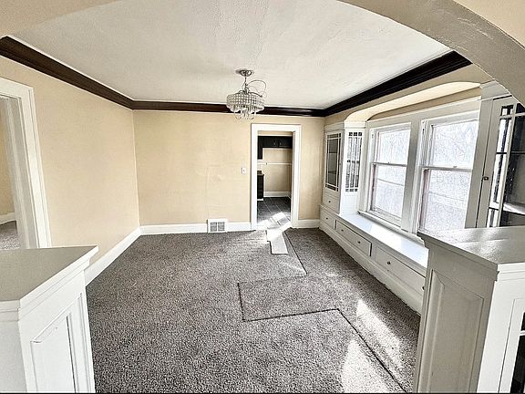Unfurnished dining area with arched walkways, dark colored carpet, a chandelier, and baseboards