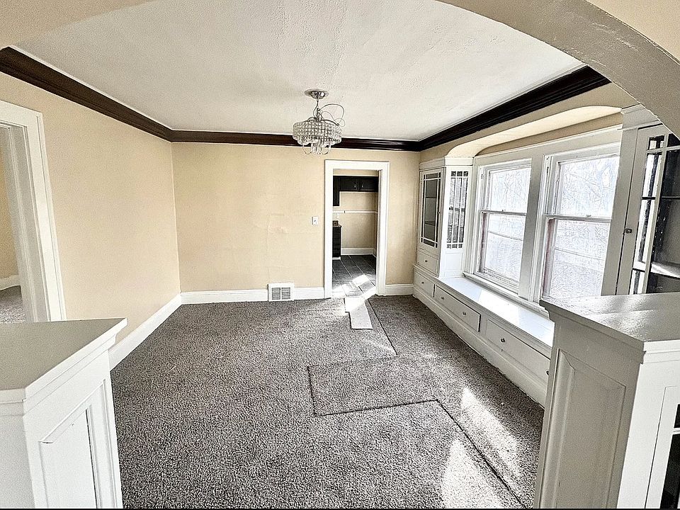 Unfurnished dining area with arched walkways, dark colored carpet, a chandelier, and baseboards