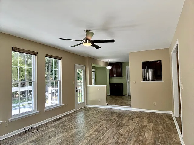 Pic from other end of living room by fireplace looking into kitchen. Half wall and step up into the kitchen and passthrough window above double kitchen sink. Pull down privacy blinds.