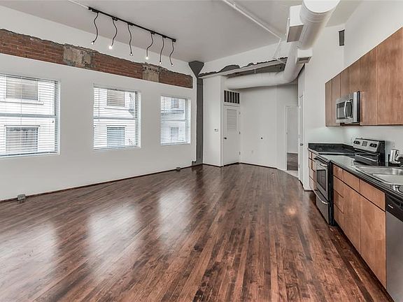 Living/Dining/Kitchen is open and features warm stained reclaimed wood floors, exposed ductwork and exposed brick above windows. Three large windows fill the space with light. Kitchen wall is on angle adding interest to the space.