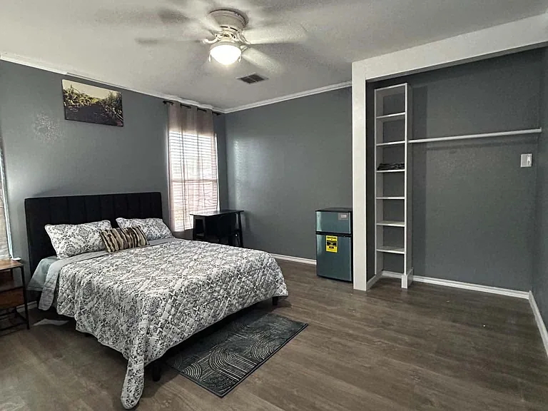 Spacious bedroom with ceiling fan, window with blinds, and open closet shelving for convenient storage.