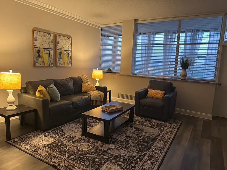 This spacious and inviting living room features beautiful wood-style flooring, large windows that provide abundant natural light, and a comfortable open layout with plenty of room for seating and entertainment.