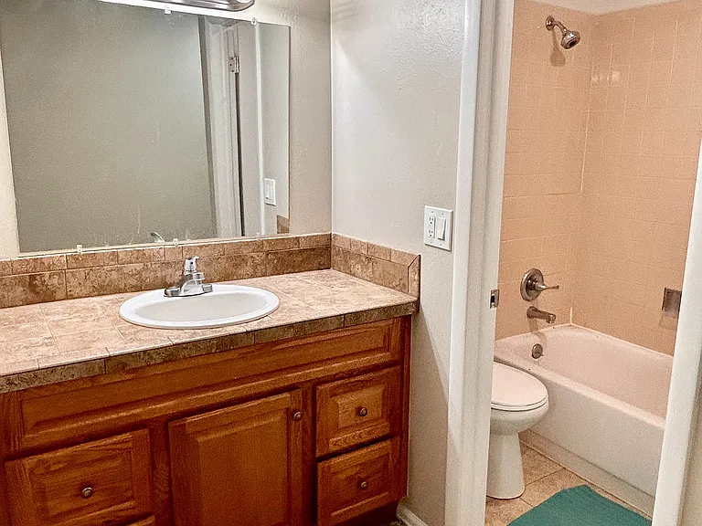 Elegant bathroom with warm wood vanity, modern lighting, and inviting bathtub in a cozy apartment.