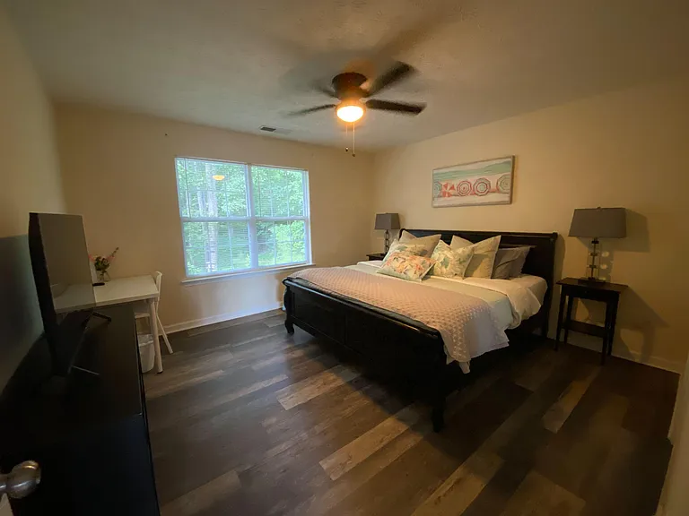 Furnished bedroom with a large window, ceiling fan, and a dedicated desk areacomfortable setup for rest and remote work.
