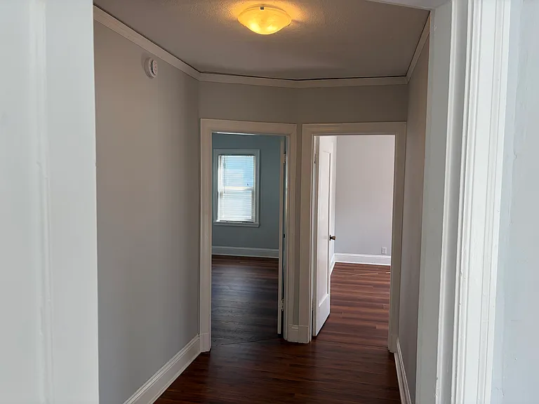 Two of the bedrooms are off a wide hallway. Each bedroom has wood laminate flooring and multiple windows.