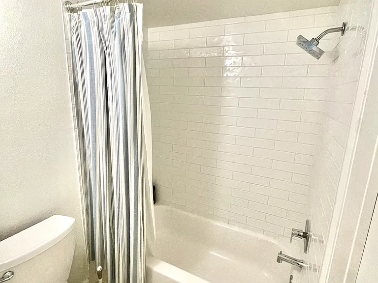 Bathroom is split into two small rooms. Pictured is toilet and shower area with ceiling fan.