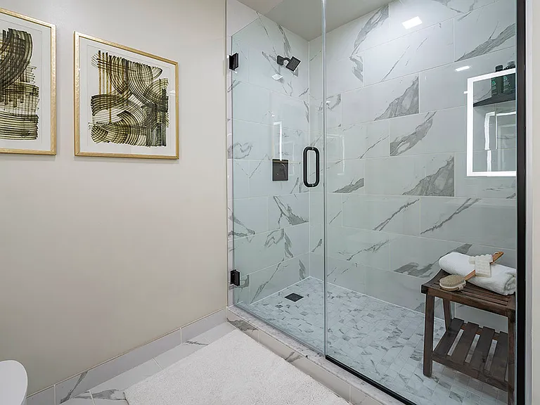 Apartment bathroom with glass-enclosed shower, tile flooring, and LED vanity mirror.