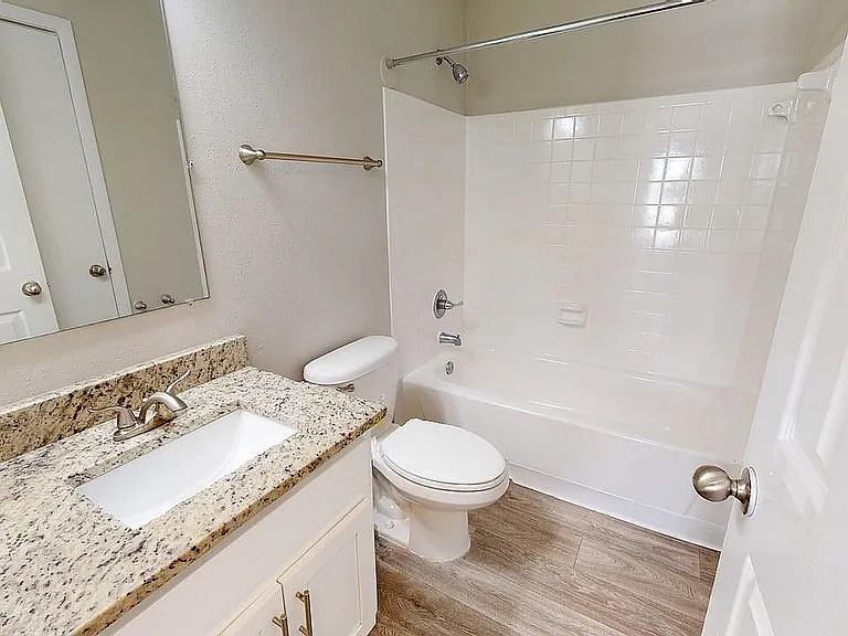 Elegant bathroom with stylish granite countertop, spacious white bathtub, and sleek wood flooring.