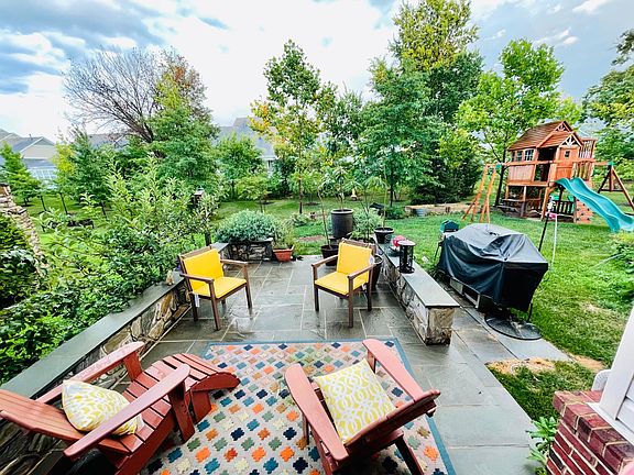 backyard with stone patio and sitting wall around for additional seating, beautiful landscape, play set, garden space. ready to fire up the grill