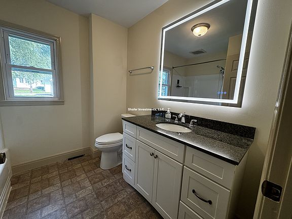 View of the bathroom with a heated, backlit mirror and cabinetry with a granite countertop.