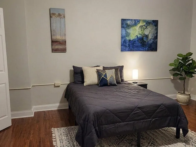 Private bedroom with hardwood floors, a full-size bed, side table lighting, and wall art, plus closet access for storage.