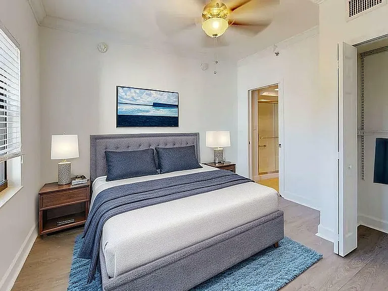 Inviting bedroom with elegant decor, featuring a plush bed, modern lighting, and a serene artwork above, complemented by ample natural light and sleek wooden flooring.
