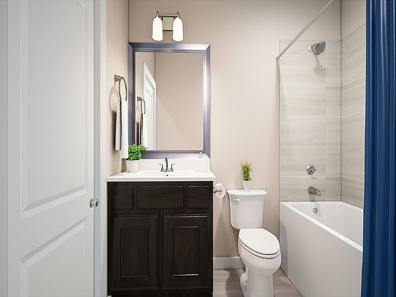 A modern bathroom with a dark wood vanity, a white toilet, and a bathtub surrounded by white walls a