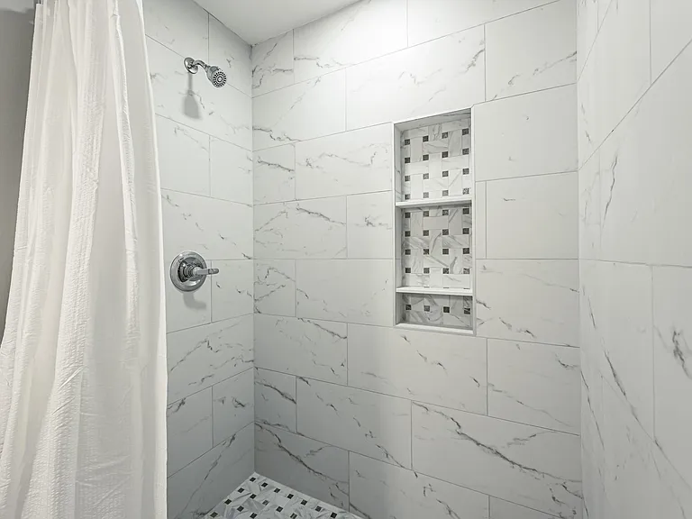 Walk-in tiled shower with rain-style showerhead, sleek fixtures, and built-in niche shelving for toiletries.