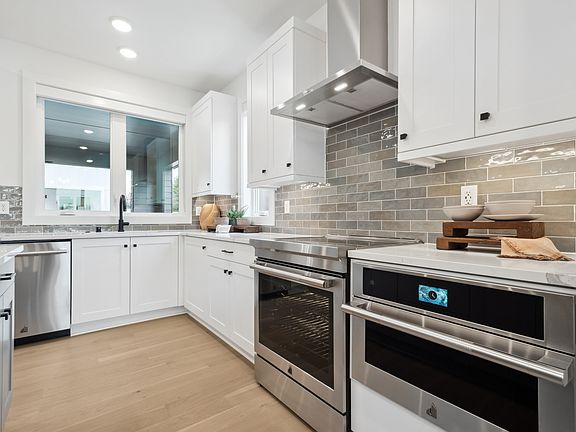 A modern, well-equipped kitchen with white cabinets, stainless steel appliances, and a tiled backspl