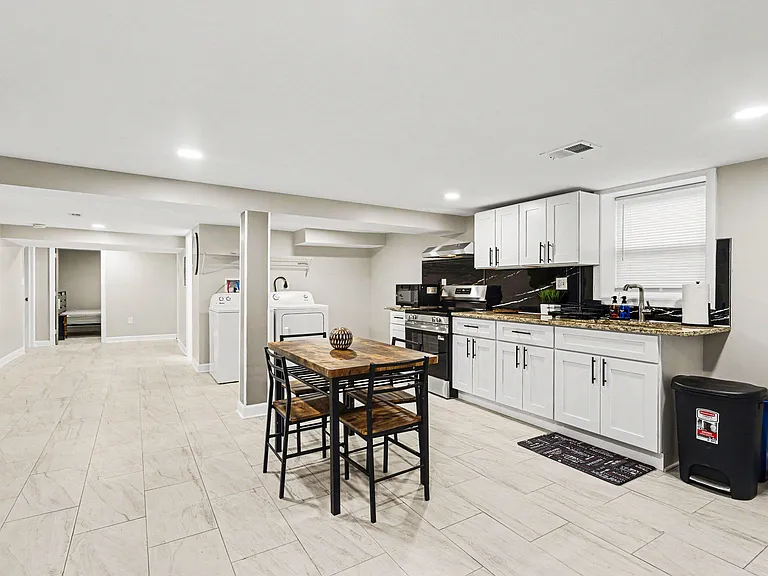 Spacious kitchen with ample white cabinetry, granite-look counters, stainless range, and a small dining table nearby.